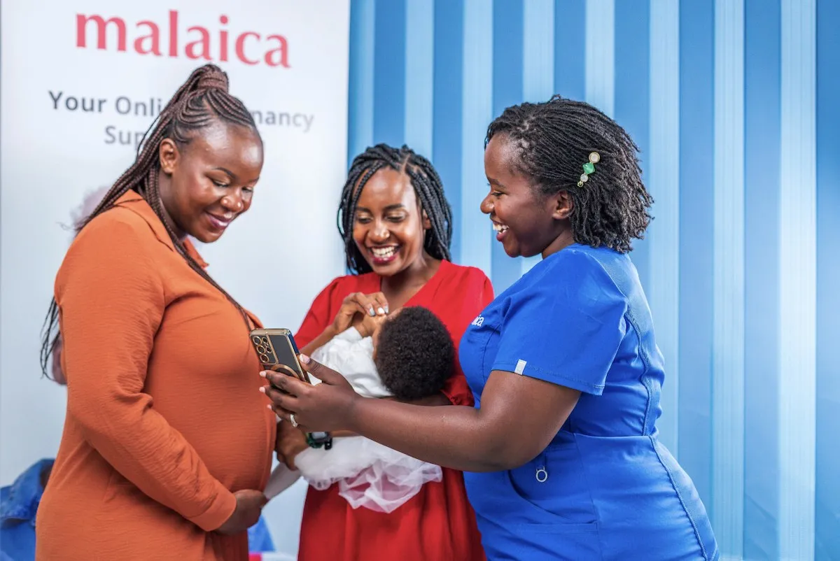 A Malaica nurse and two mothers looking at a phone together